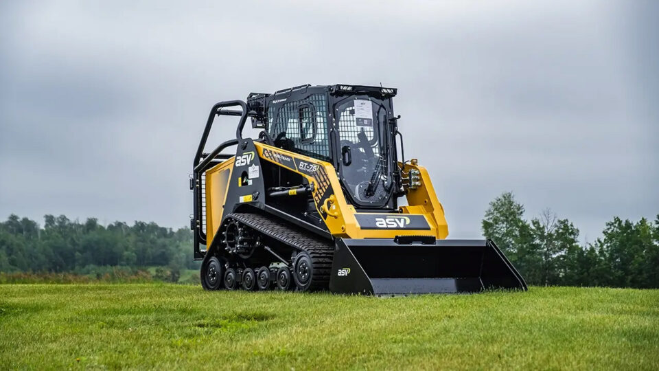 Yellow compact track loader on grassy field.