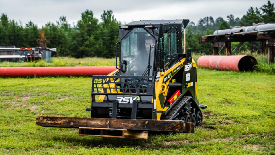 Compact track loader carrying wooden log outdoors