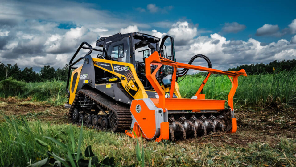 Forestry tractor clearing land under cloudy sky.
